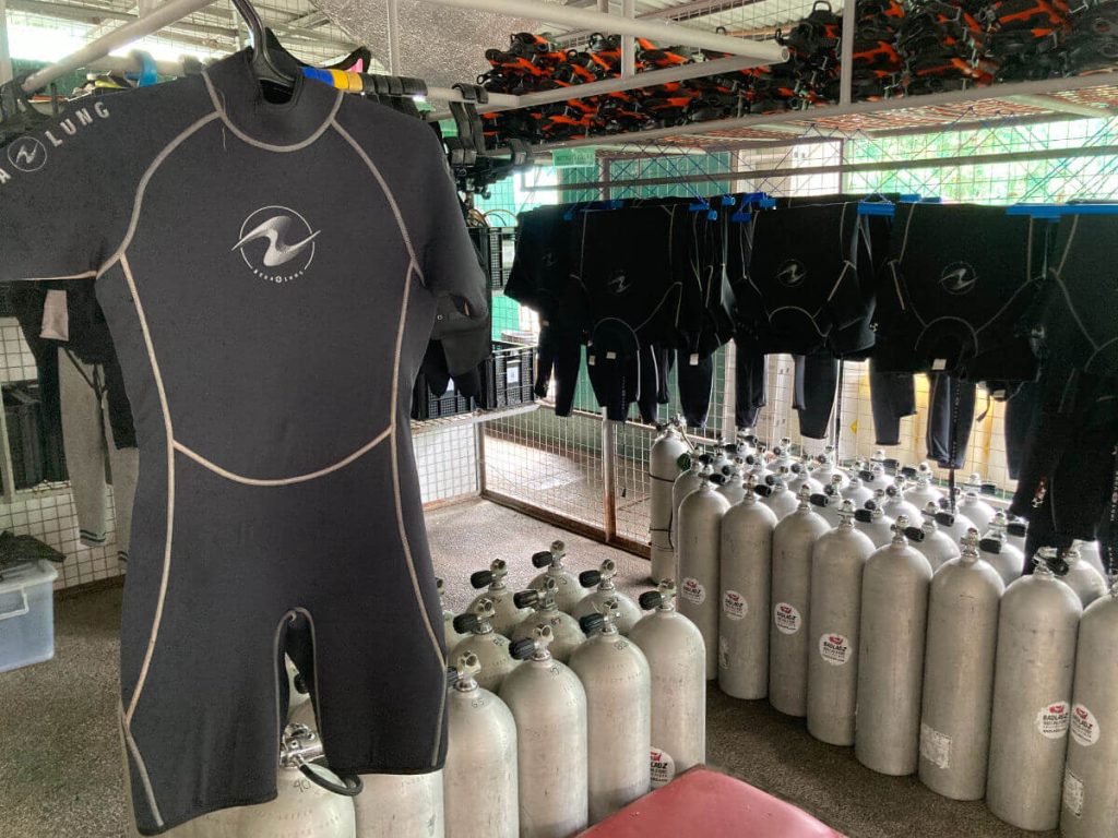 A Black aqualung wetsuit that stops just above the knees and elbows hanging in a diving equipment room