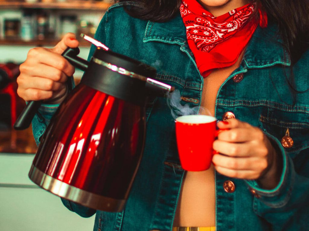 Woman holding a red kettle pouring hot water into a red mug