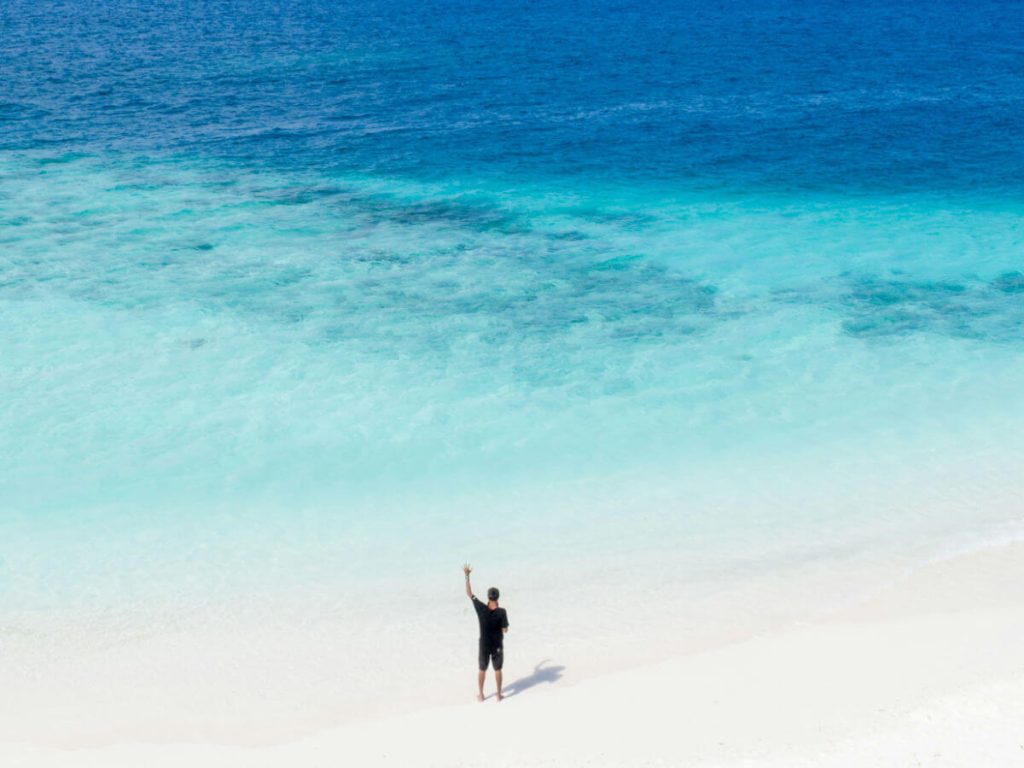 A Man standing on the edge of a beach waving out to sea