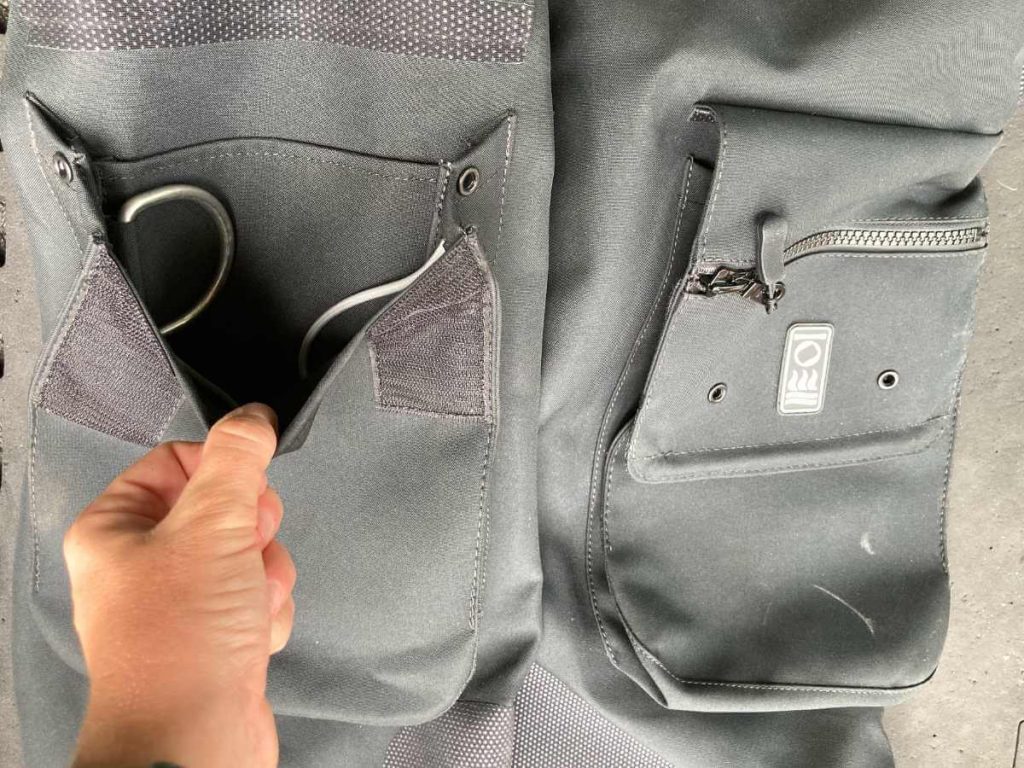 A Hand holding open a pair of Fourth Element drysuit leg pockets