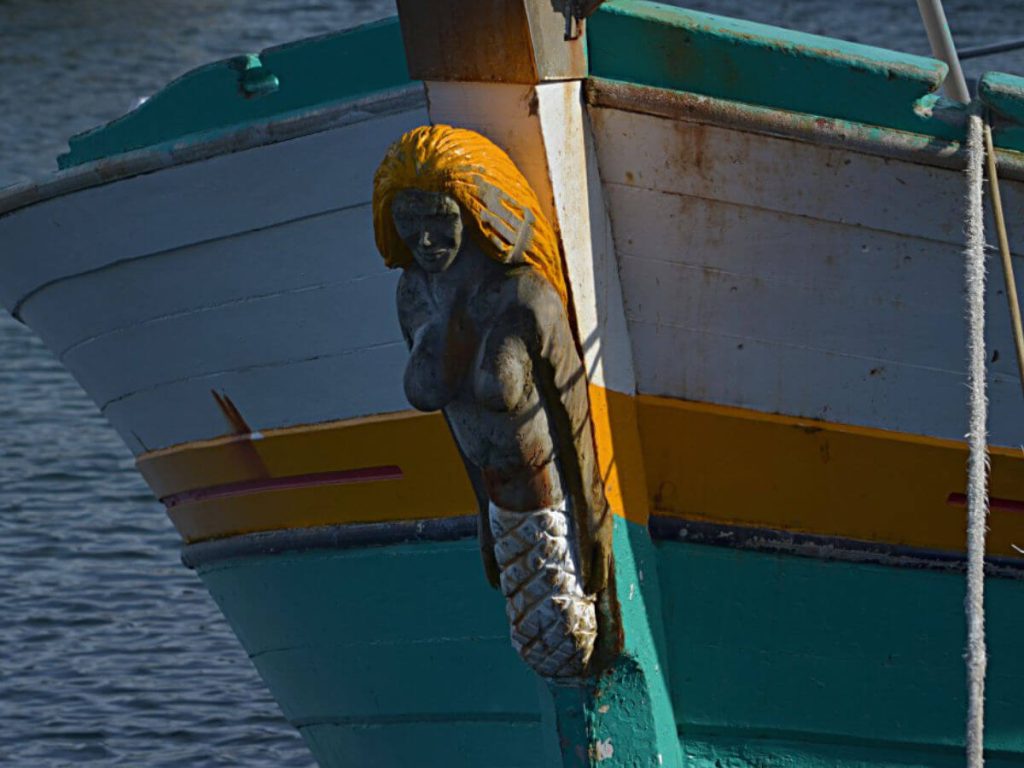 A teal and yellow boat with a yellow haired mermaid as a figurehead