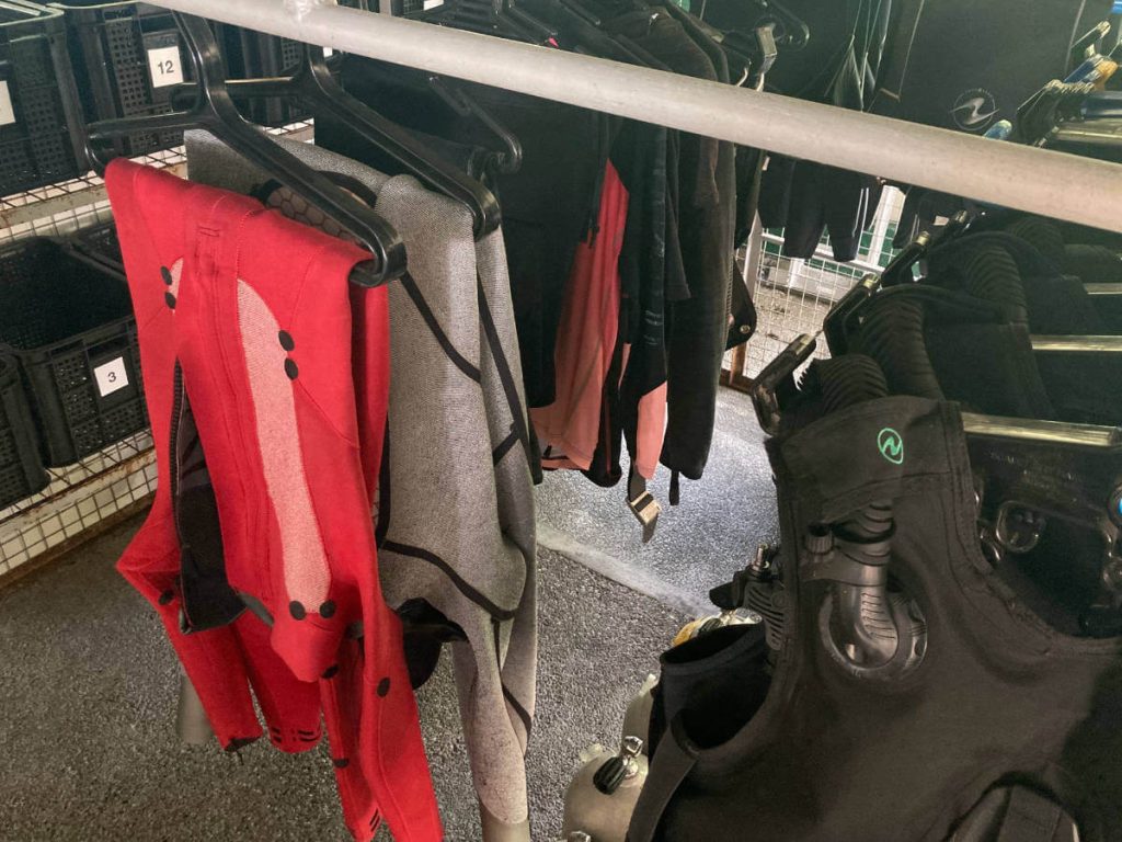 Wetsuits hanging inside out folded over at the waist on thick black hangars