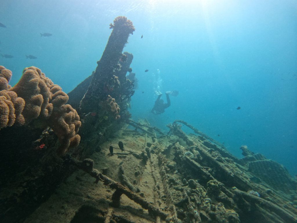 A scuba diver hovering above the twisted metal of a small shipwreck on million dollar point