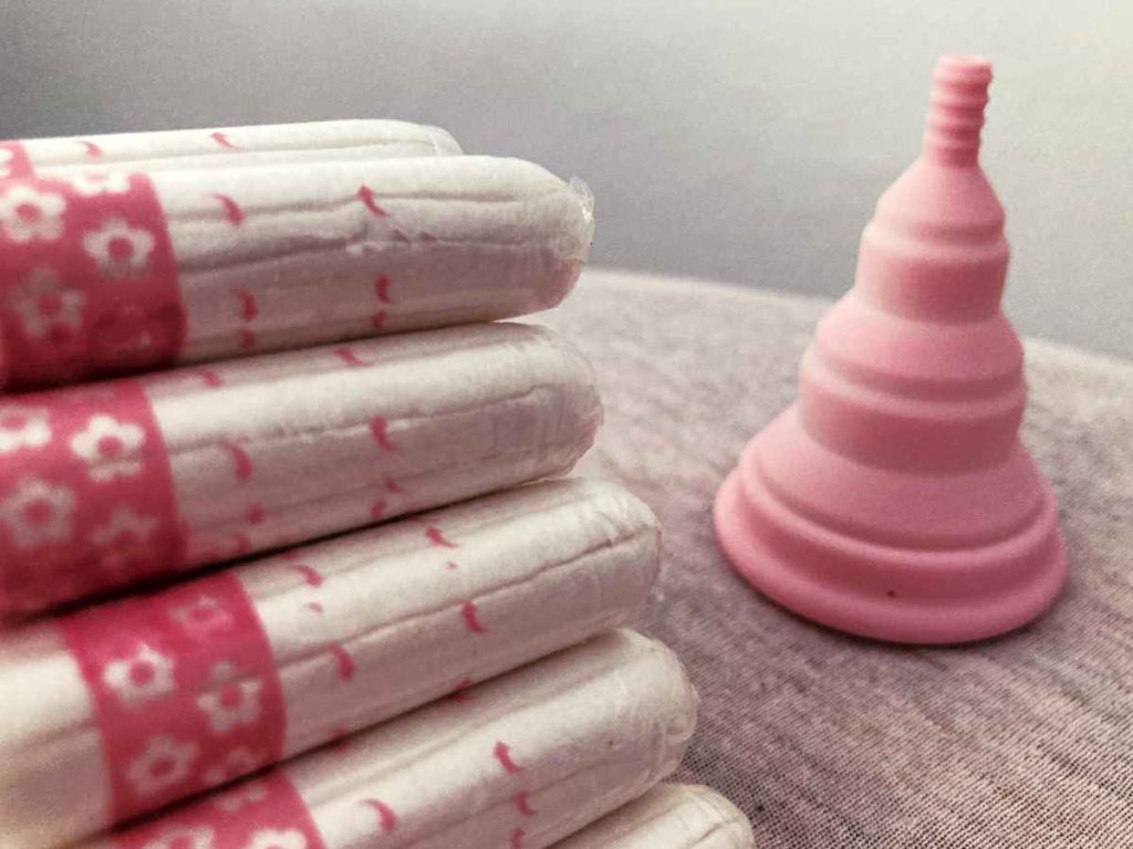 Pink Lily cup compact menstrual cups on a table next to a pile of pink tampons