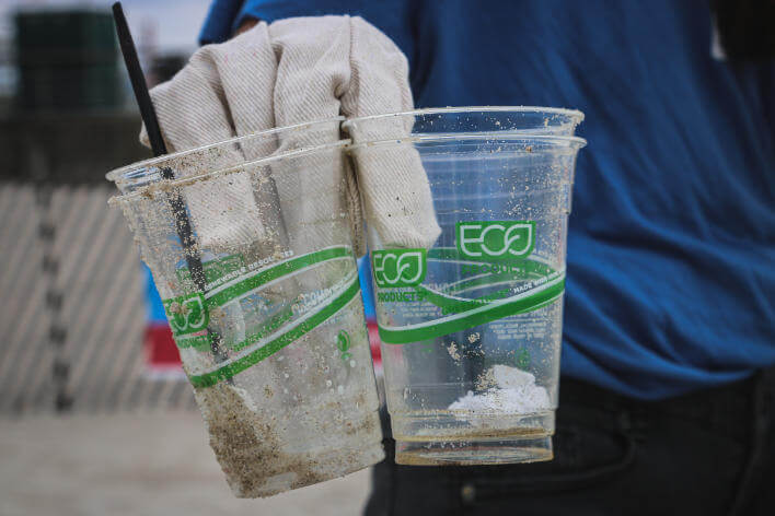 A Litter picker holding up two clear plastic cups with 'eco' written in green in on them