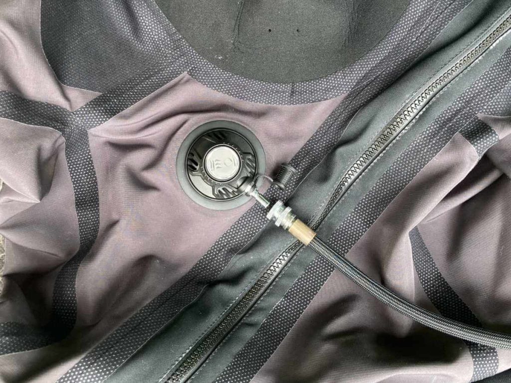 A drysuit inflator valve in the middle of the chest with an inflator hose attached