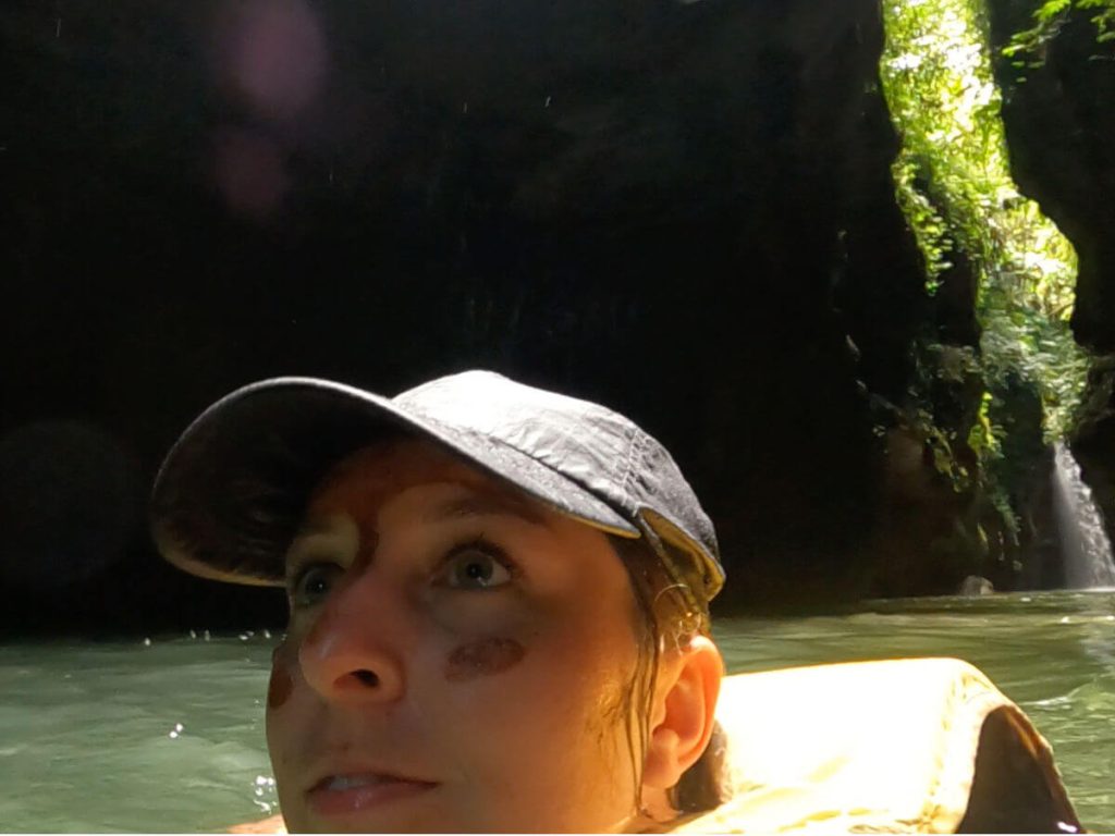 Woman swimming in a canyon wearing a black baseball cap
